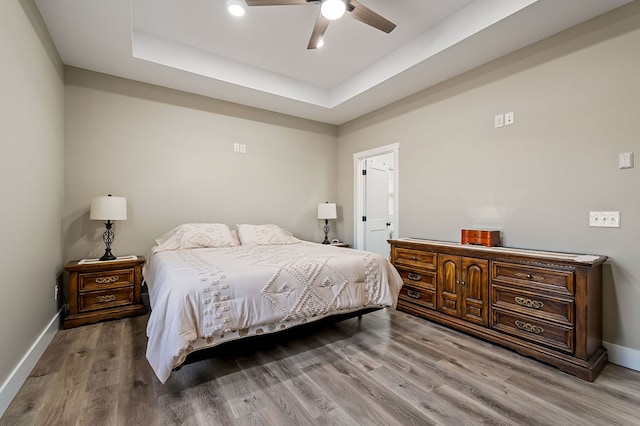 bedroom with a tray ceiling, baseboards, wood finished floors, and a ceiling fan