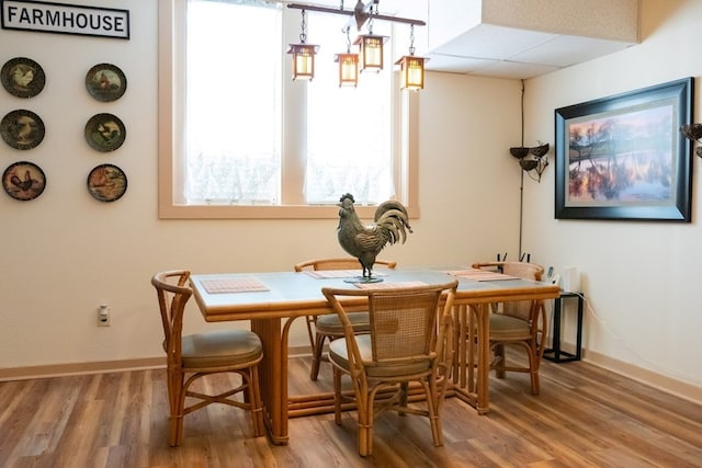 dining area with a drop ceiling, baseboards, and wood finished floors