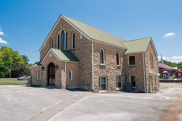 view of front of home with stone siding, central AC unit, and metal roof