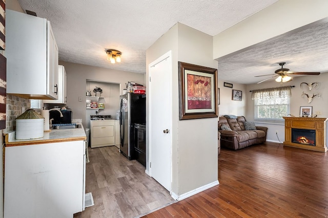 kitchen featuring open floor plan, wood finished floors, a lit fireplace, light countertops, and a sink