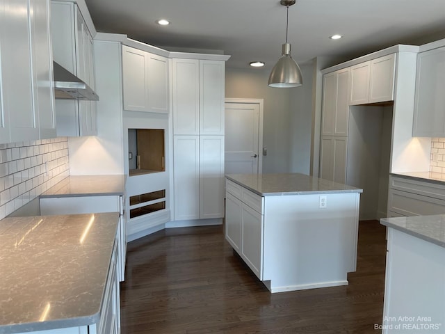 kitchen with a center island, light stone countertops, tasteful backsplash, decorative light fixtures, and white cabinetry