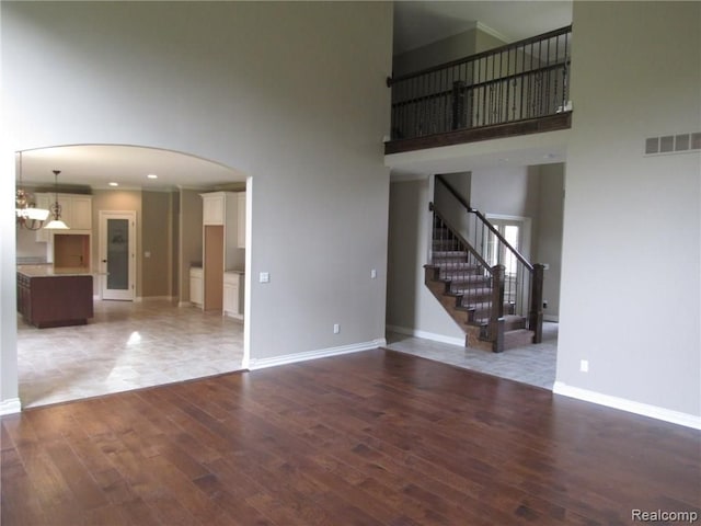 unfurnished living room with hardwood / wood-style flooring, a notable chandelier, and a towering ceiling