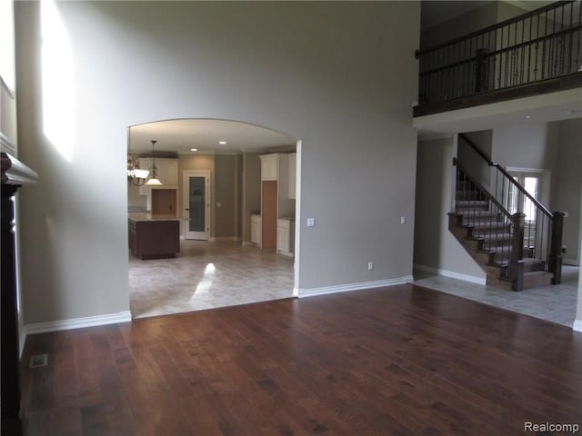 unfurnished living room with a towering ceiling, dark wood-type flooring, and an inviting chandelier