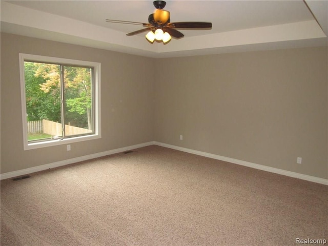 carpeted spare room with ceiling fan and a raised ceiling