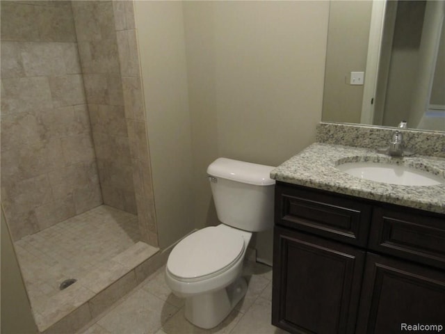 bathroom featuring tile patterned flooring, vanity, toilet, and tiled shower