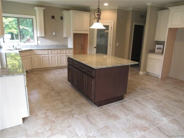 kitchen with light stone countertops, ornamental molding, pendant lighting, cream cabinets, and a kitchen island