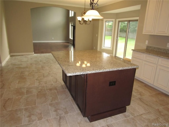 kitchen featuring light stone counters, dark brown cabinetry, a notable chandelier, a center island, and hanging light fixtures