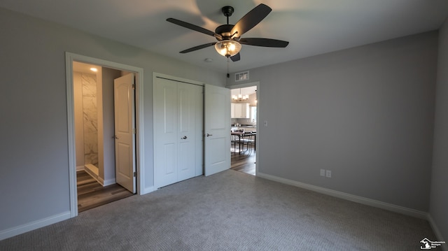 unfurnished bedroom with dark colored carpet, ceiling fan with notable chandelier, ensuite bathroom, and a closet