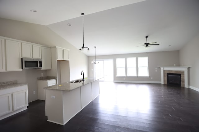 kitchen featuring ceiling fan with notable chandelier, vaulted ceiling, a kitchen island with sink, white cabinets, and hanging light fixtures