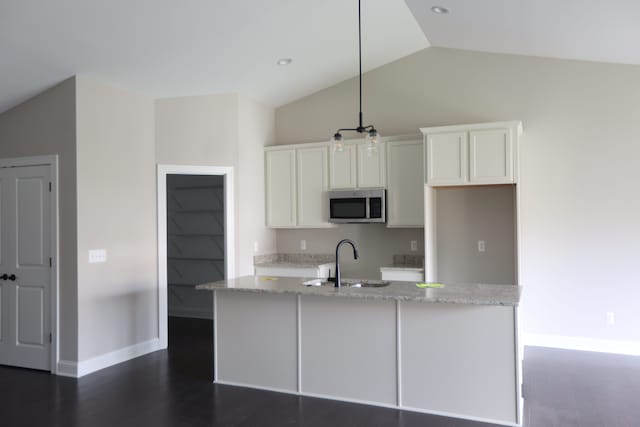 kitchen featuring lofted ceiling, sink, hanging light fixtures, light stone counters, and white cabinetry