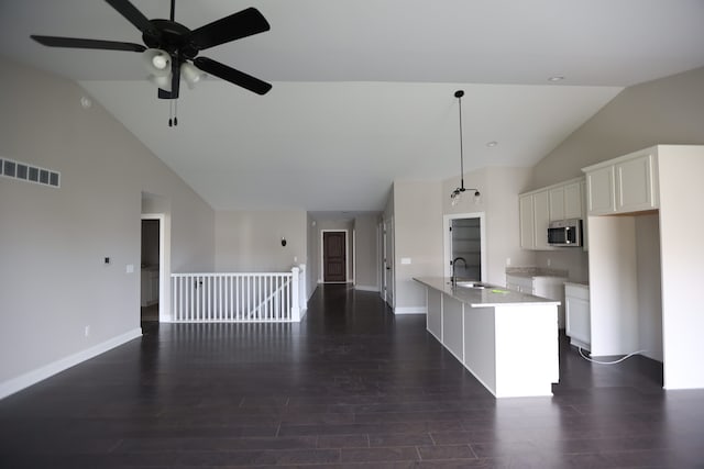 kitchen with dark wood-type flooring, sink, white cabinetry, hanging light fixtures, and an island with sink