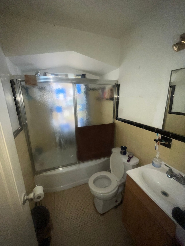 full bathroom featuring tile patterned flooring, combined bath / shower with glass door, toilet, vanity, and tile walls