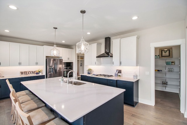 kitchen featuring appliances with stainless steel finishes, a center island with sink, wall chimney exhaust hood, and sink