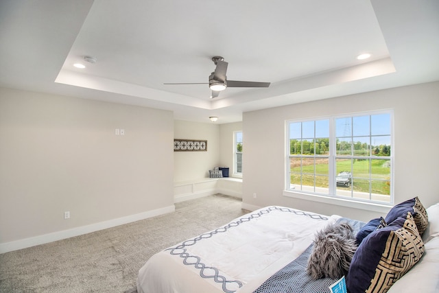 carpeted bedroom with a raised ceiling and ceiling fan