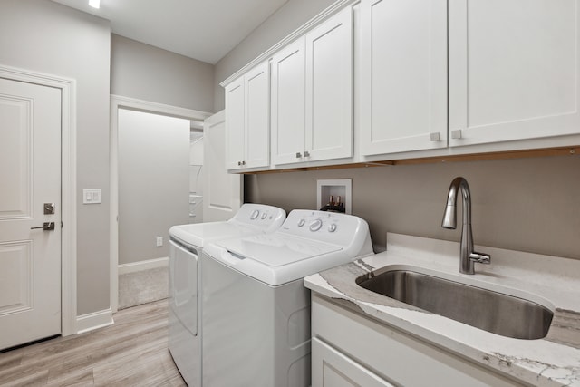 laundry area with cabinets, sink, washer and dryer, and light hardwood / wood-style flooring