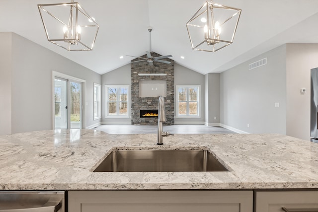 kitchen featuring pendant lighting, a stone fireplace, light stone countertops, and sink