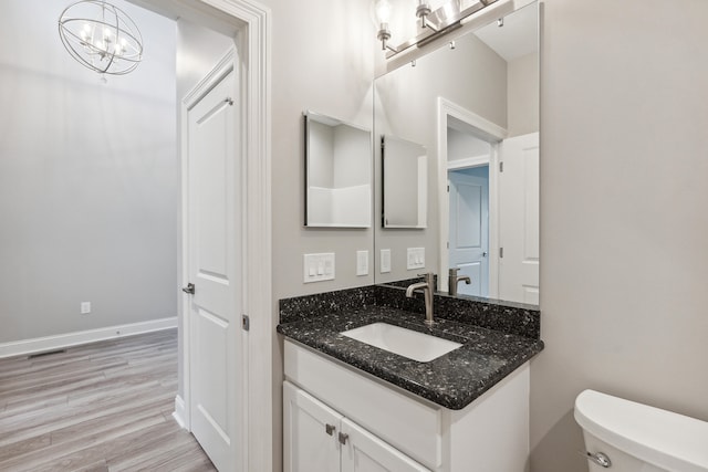 bathroom with hardwood / wood-style flooring, vanity, toilet, and an inviting chandelier