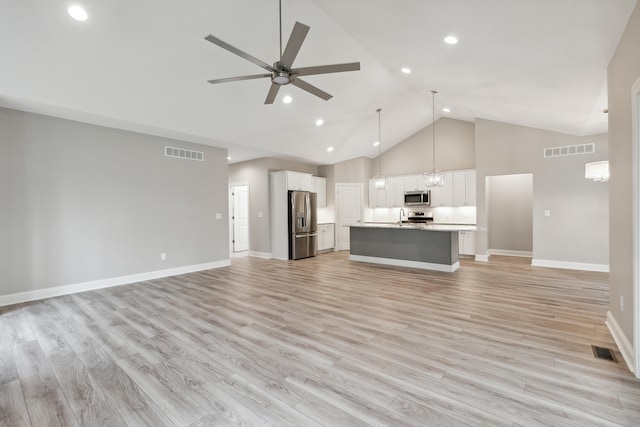 unfurnished living room with ceiling fan with notable chandelier, high vaulted ceiling, and light hardwood / wood-style flooring