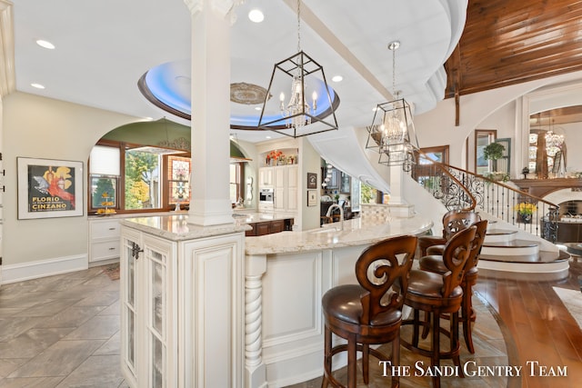 bar featuring light stone counters, a tray ceiling, decorative light fixtures, dark hardwood / wood-style floors, and white cabinetry