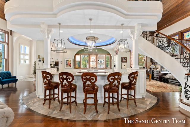 bar with a tray ceiling, light stone counters, hanging light fixtures, and dark wood-type flooring