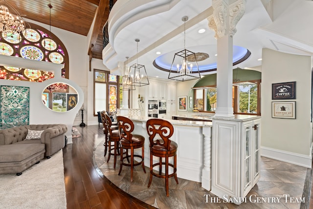 bar featuring pendant lighting, dark hardwood / wood-style floors, light stone counters, white cabinetry, and decorative columns