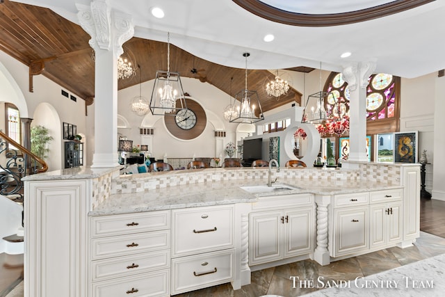 kitchen with light stone counters, ornate columns, sink, white cabinetry, and hanging light fixtures