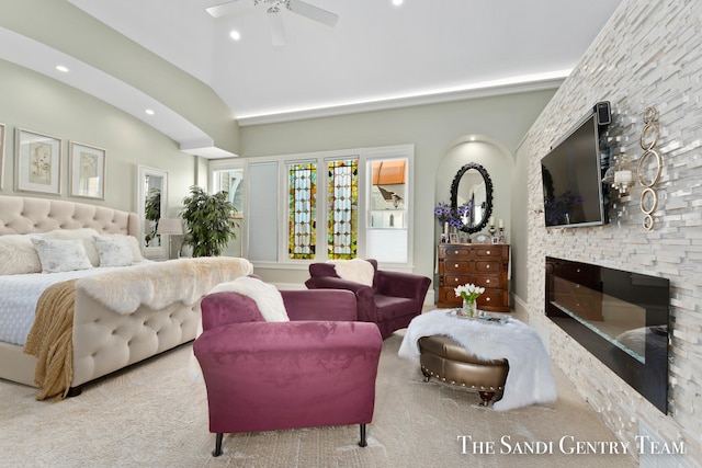 carpeted bedroom with ceiling fan, a stone fireplace, and vaulted ceiling