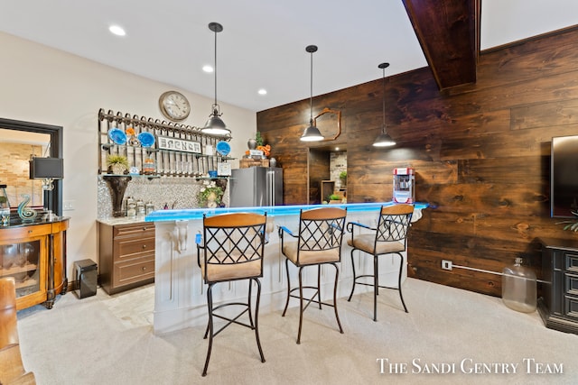 bar featuring hanging light fixtures, wooden walls, backsplash, stainless steel fridge, and light carpet