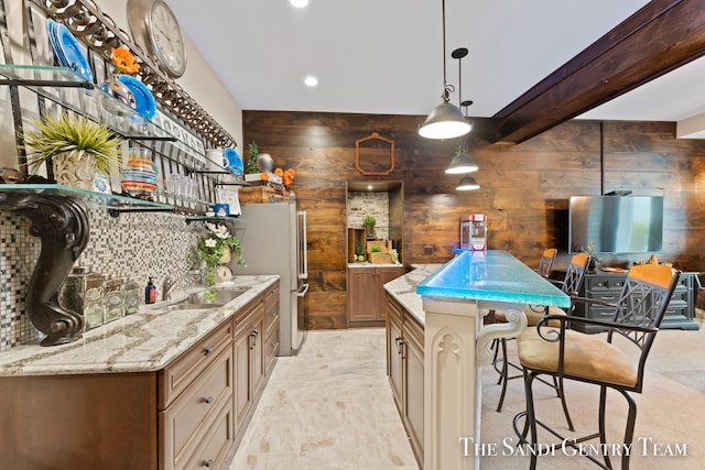 bar featuring sink, wooden walls, light stone countertops, beamed ceiling, and decorative light fixtures