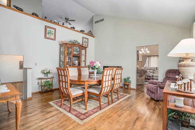 dining space with hardwood / wood-style floors, high vaulted ceiling, and ceiling fan with notable chandelier