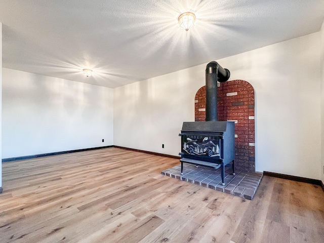 unfurnished living room featuring a wood stove, light hardwood / wood-style floors, and a textured ceiling