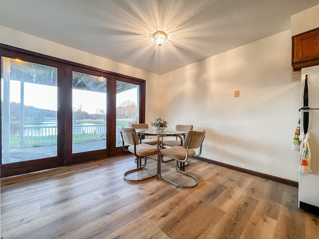 dining space with light hardwood / wood-style flooring, a water view, and french doors