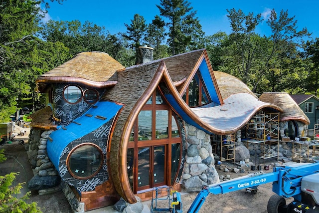 9554 Fowler Ln, Rapid City, MI 49676 - view of home's exterior featuring stone siding, view of wooded area, and a chimney