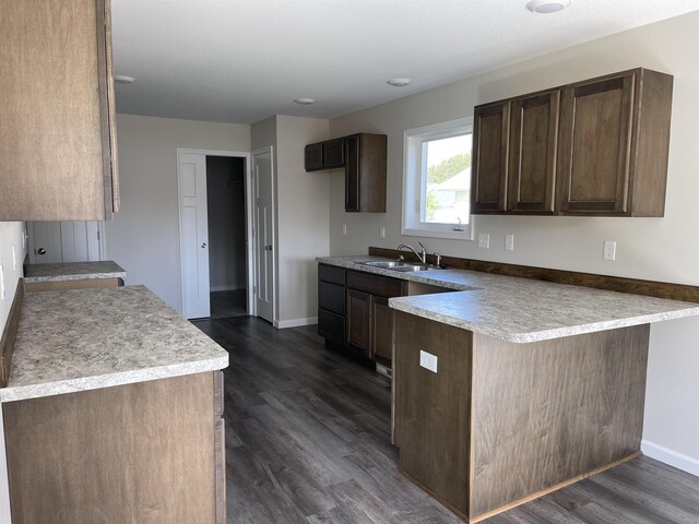 260 Windemere Pl, West Branch, MI 48661 - kitchen featuring a peninsula, a sink, dark brown cabinets, dark wood-type flooring, and baseboards