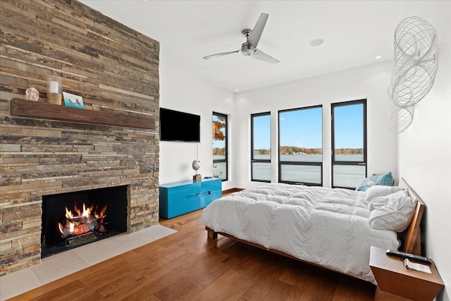 bedroom featuring access to outside, a stone fireplace, ceiling fan, and hardwood / wood-style floors