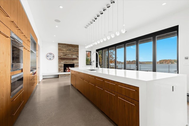 kitchen featuring a large fireplace, sink, pendant lighting, a water view, and a large island