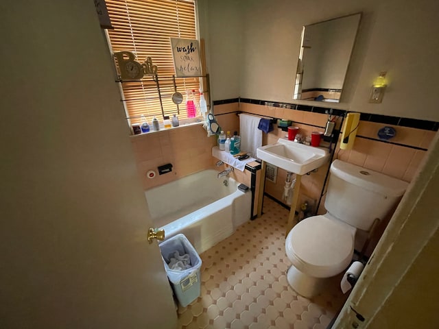 bathroom with a tub to relax in, sink, tile walls, and toilet