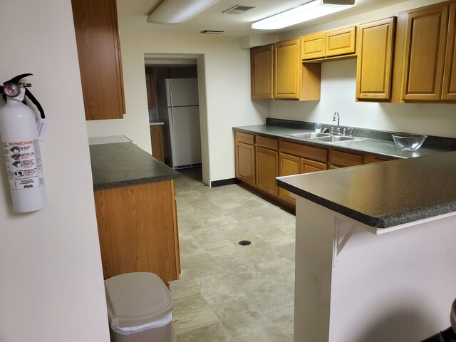 20331 Outer Dr, Dearborn, MI 48124 - kitchen with freestanding refrigerator, a sink, dark countertops, a peninsula, and brown cabinets