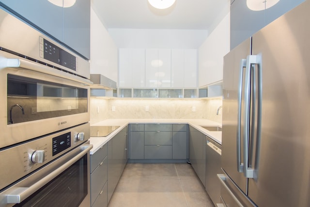 kitchen with appliances with stainless steel finishes, wall chimney range hood, sink, light tile patterned floors, and white cabinets