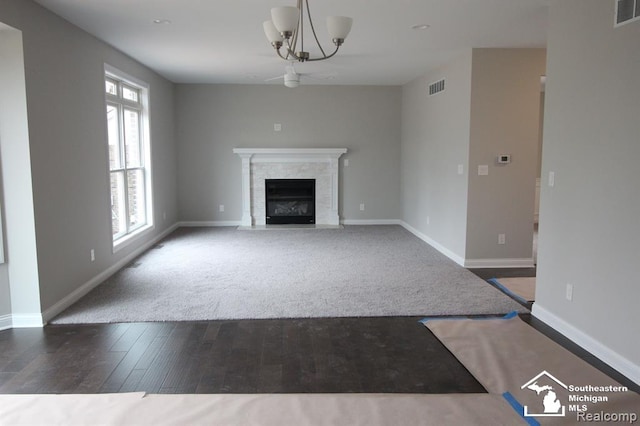 unfurnished living room featuring ceiling fan with notable chandelier and dark hardwood / wood-style floors