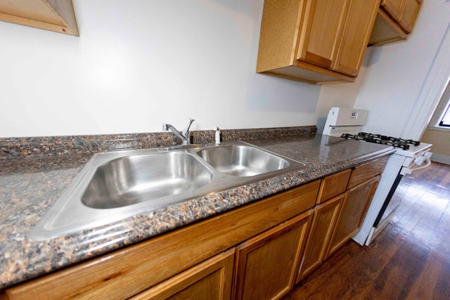 kitchen with white gas range oven, dark hardwood / wood-style floors, dark stone counters, and sink