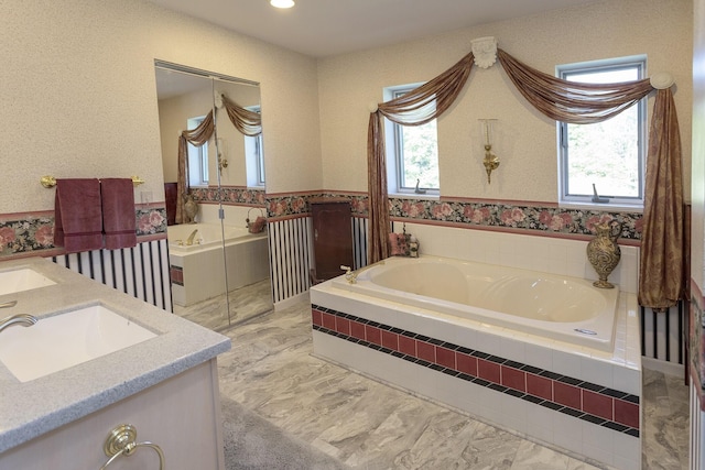 bathroom with a relaxing tiled tub, vanity, and a healthy amount of sunlight