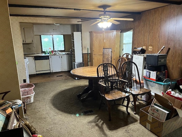 carpeted dining area with beam ceiling, wood walls, and ceiling fan