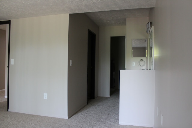 corridor with light colored carpet and a textured ceiling