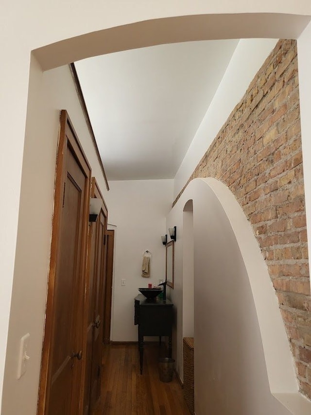 hallway with dark hardwood / wood-style flooring and brick wall