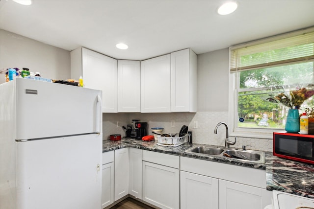 kitchen with decorative backsplash, dark stone counters, sink, white cabinets, and white fridge