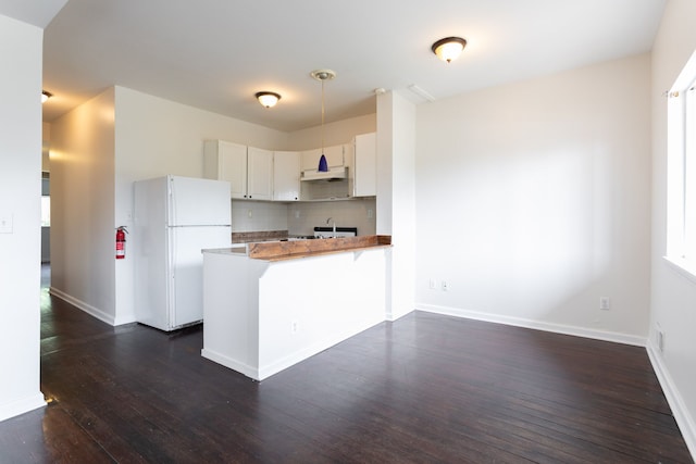 kitchen with tasteful backsplash, dark hardwood / wood-style flooring, kitchen peninsula, white fridge, and white cabinets