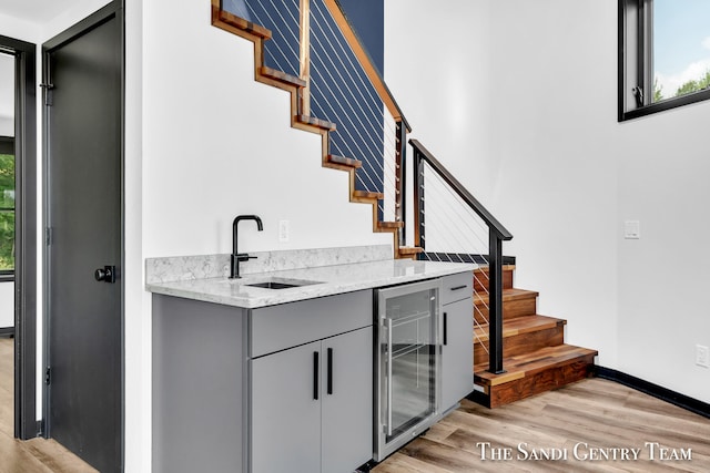 bar featuring gray cabinetry, light wood-type flooring, sink, and beverage cooler