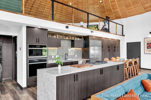 kitchen featuring stacked washing maching and dryer, stainless steel appliances, high vaulted ceiling, wooden ceiling, and a kitchen island