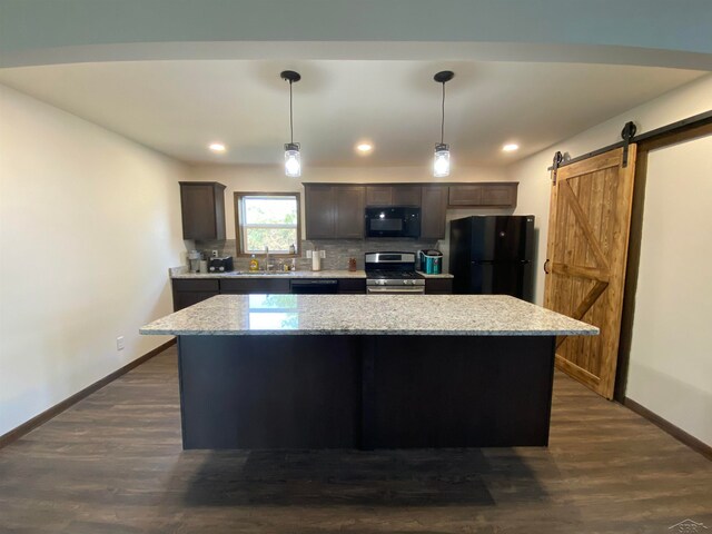 kitchen featuring dark brown cabinetry, black appliances, a barn door, decorative light fixtures, and a center island